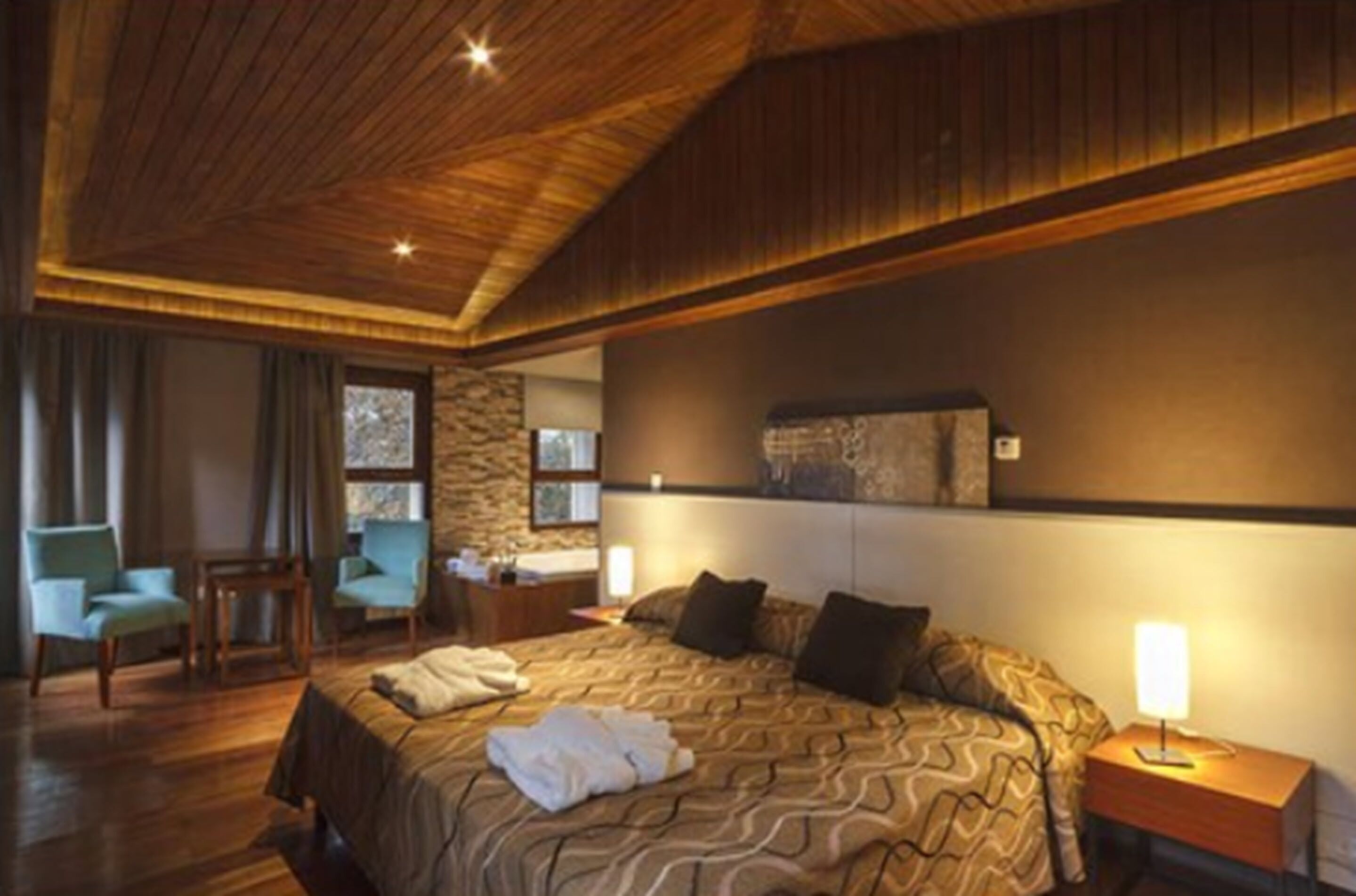 Ein Hotelzimmer mit einem großen Bett, einer Holzzahlende, einer Wand aus Stein und einem Schreibtisch mit Stuhl.