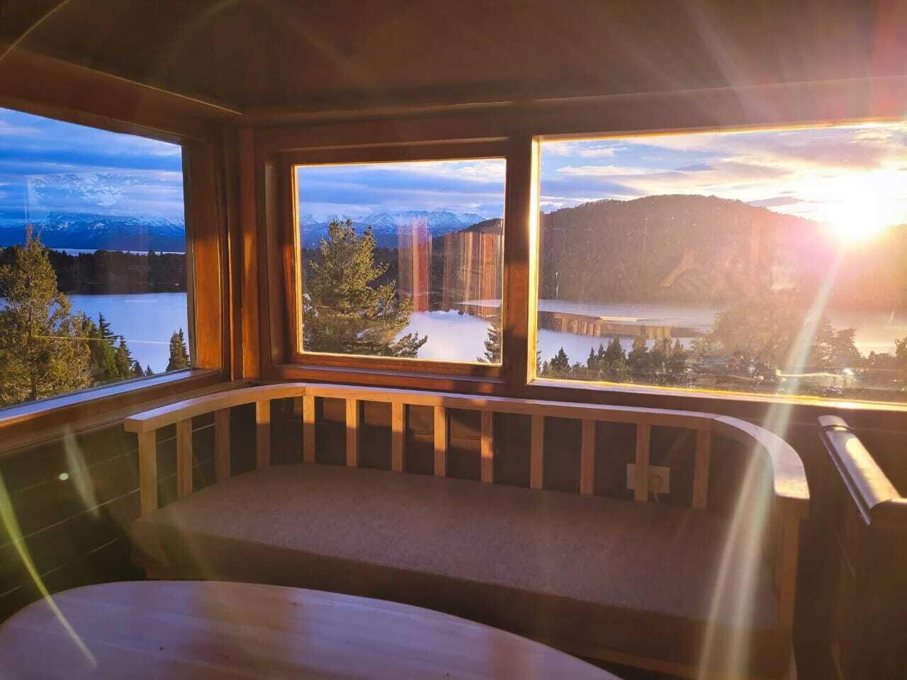 A room with a wooden bench and large windows offering a view of a snowy landscape and mountains.