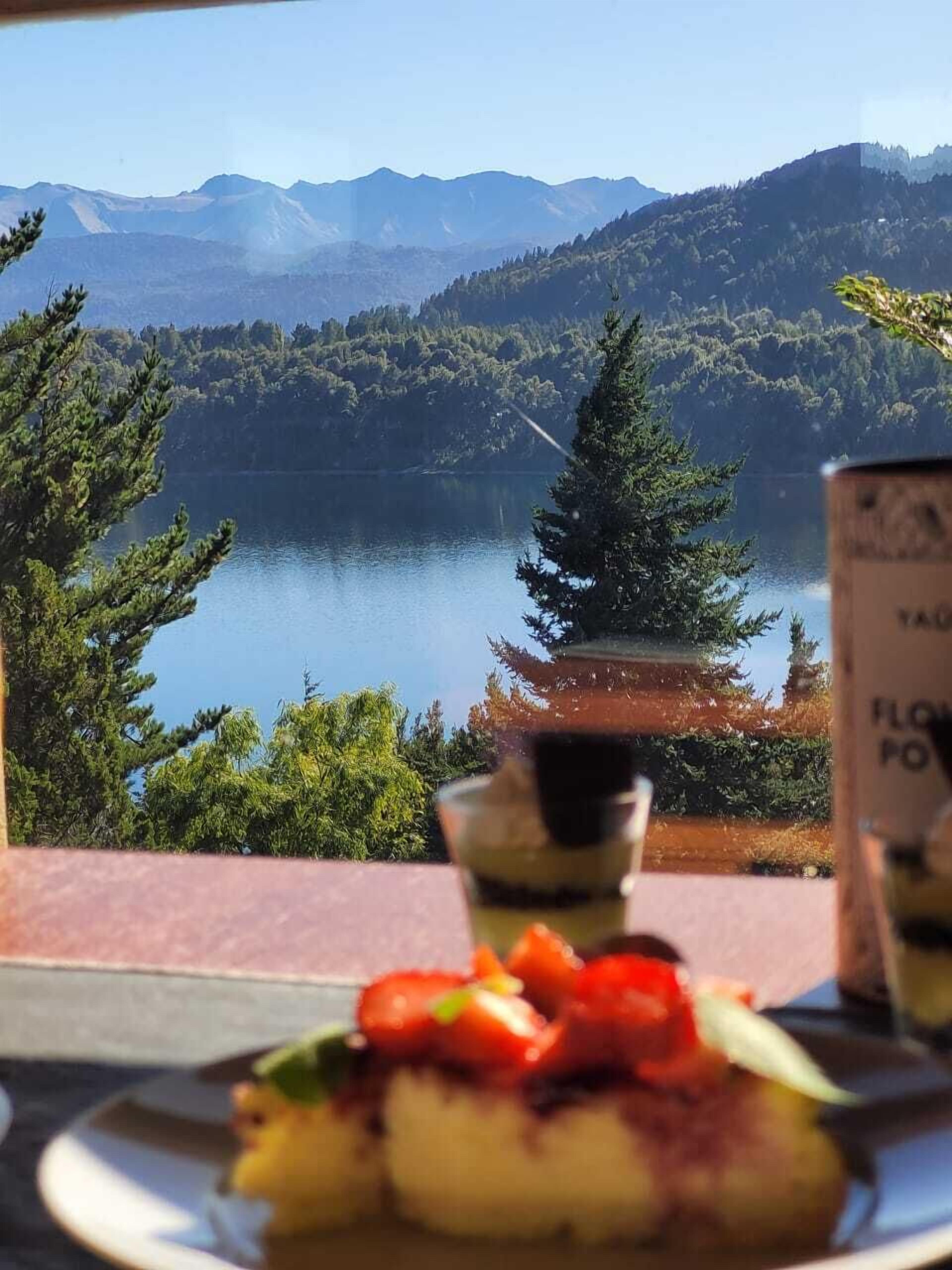A scenic view of a lake with mountains in the background, a traditional building, and a table with food.