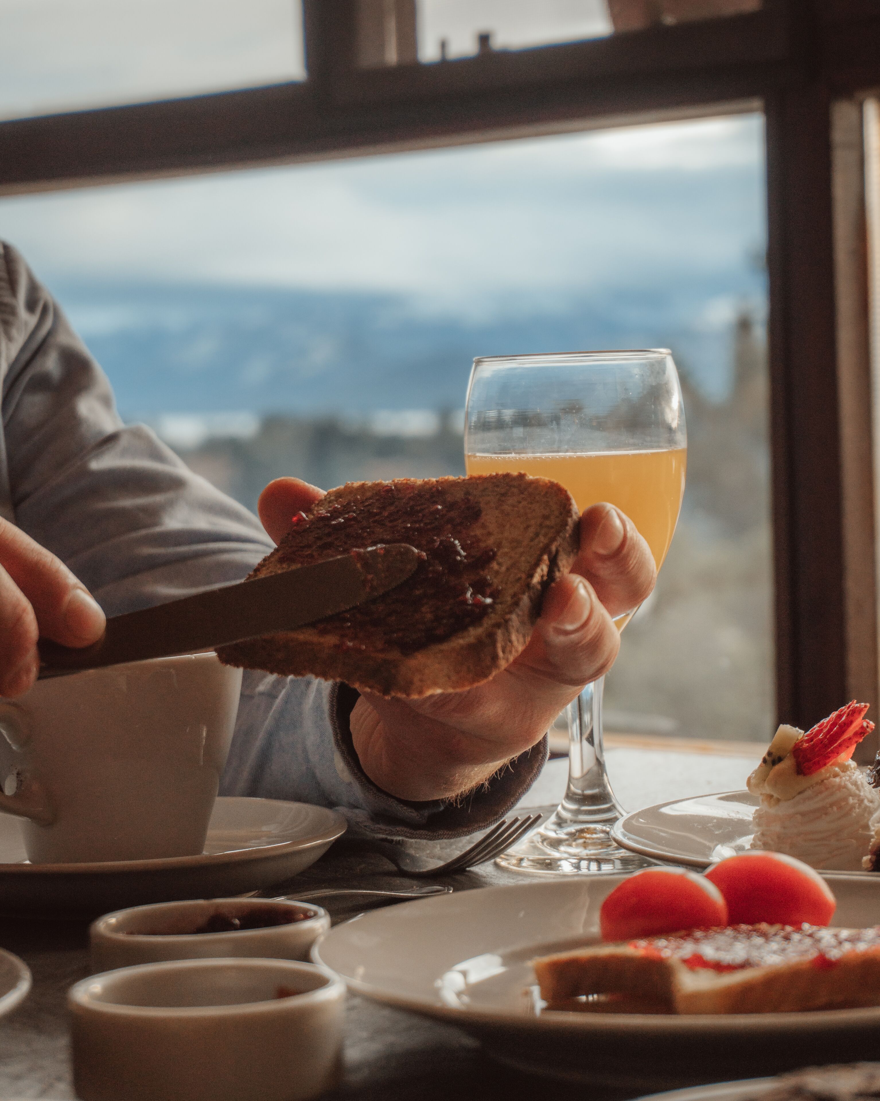 Une personne tenant une tranche de pain grillé tartinée de confiture, un verre de jus d’orange et une assiette contenant un dessert aux fraises.