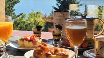 Ein Frühstückstisch mit Blick auf einen idyllischen See, mit einem Croissant, Obst und einem Getränk.