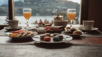 Une table garnie de diverses pâtisseries, de verres de jus d’orange et offrant une vue pittoresque sur les montagnes par la fenêtre.