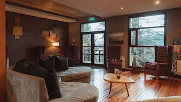 A spacious lobby with a wooden floor, large windows, and a mix of seating including sofas and armchairs.