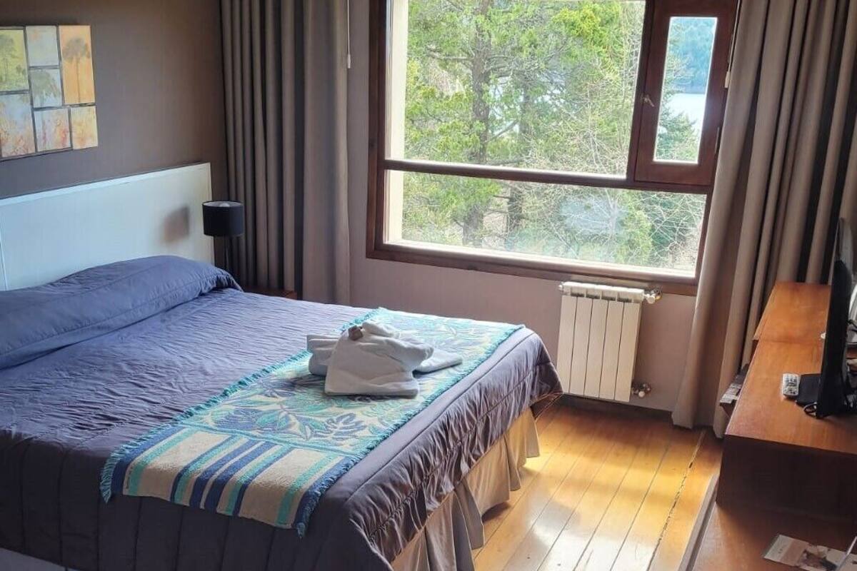 A bedroom with a bed, a window with curtains, a radiator, and a wooden floor.