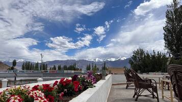 A terrace with a view of snow-capped mountains, a flower bed with red and white flowers, and wooden furniture.
