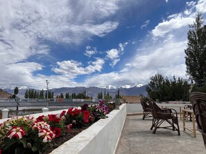 A terrace with a view of snow-capped mountains, a flower bed with red and white flowers, and wooden furniture. - Hotel New Glacier View (Leh)