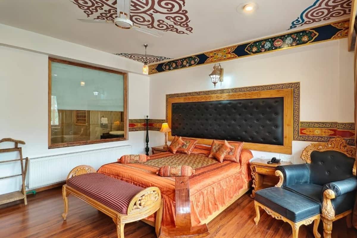 A spacious bedroom with a large bed, a wooden bench, a chair, and a window with a view of the outside.
