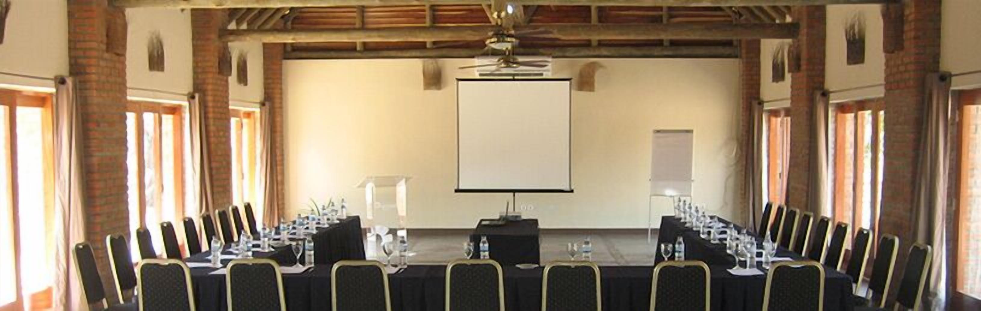 A conference room with a long table, chairs, a podium, and a projector screen.