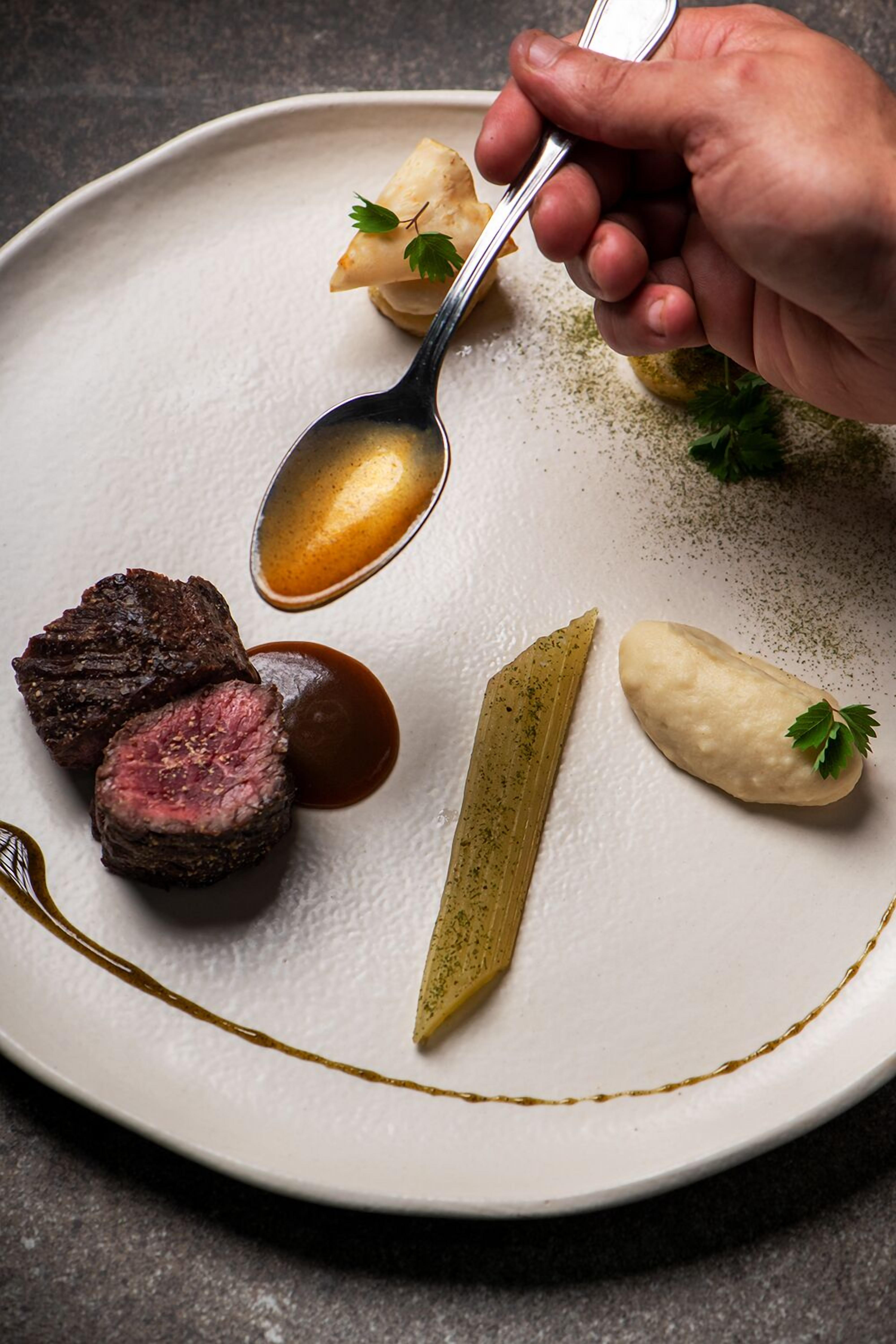 A plate with a steak, pickles, and a sauce.