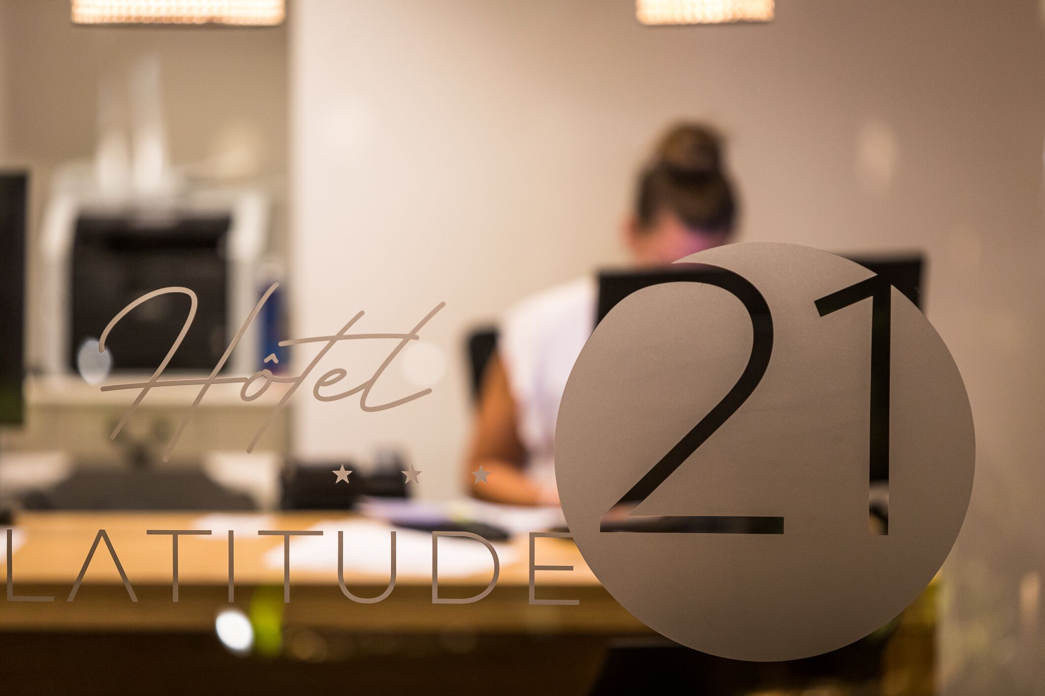 A hotel reception desk with a large number '21' sign and the words 'Hotel LATITUDE' visible.