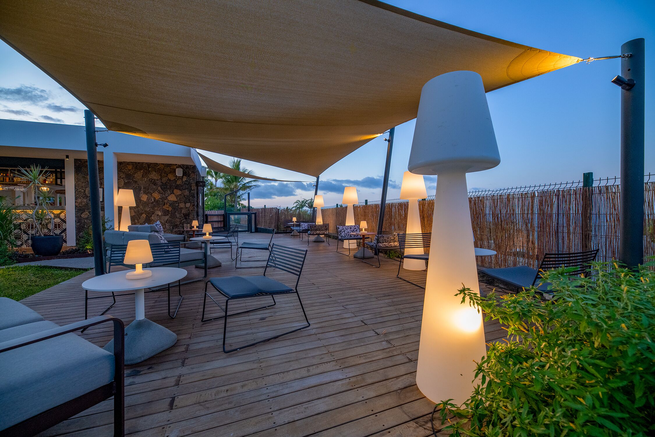 En udendørs terrasse med trægulv, borde, stole og lamper.