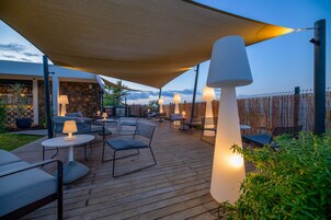Un patio al aire libre con piso de madera, mesas, sillas y lámparas.