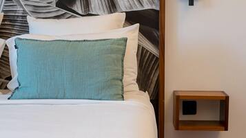 Una cama bien hecha con un almohá de color turquesa, una lámpara negra fijada a la pared y una mesita de noche de madera.