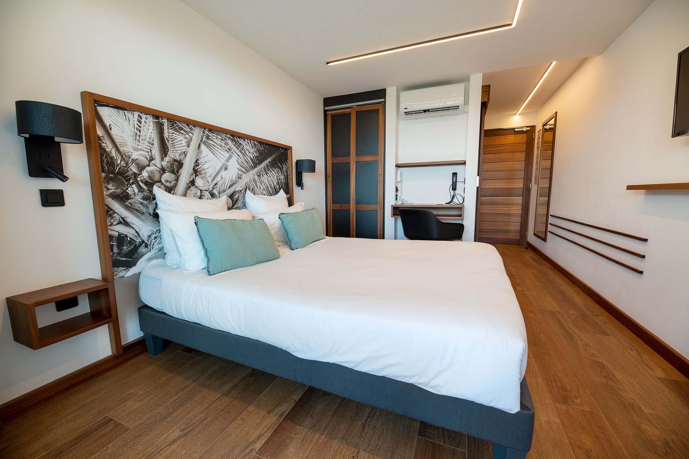 A modern hotel room with a large bed, a desk, and a wardrobe.