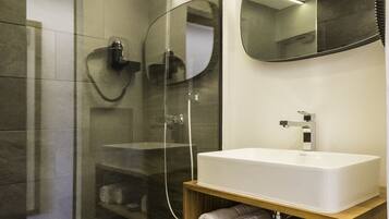 Un baño moderno con ducha de vidrio, un lavabo blanco y un mueble de tocador de madera con toallas.