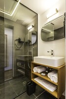 Un baño moderno con ducha de vidrio, un lavabo blanco y un mueble de tocador de madera con toallas.