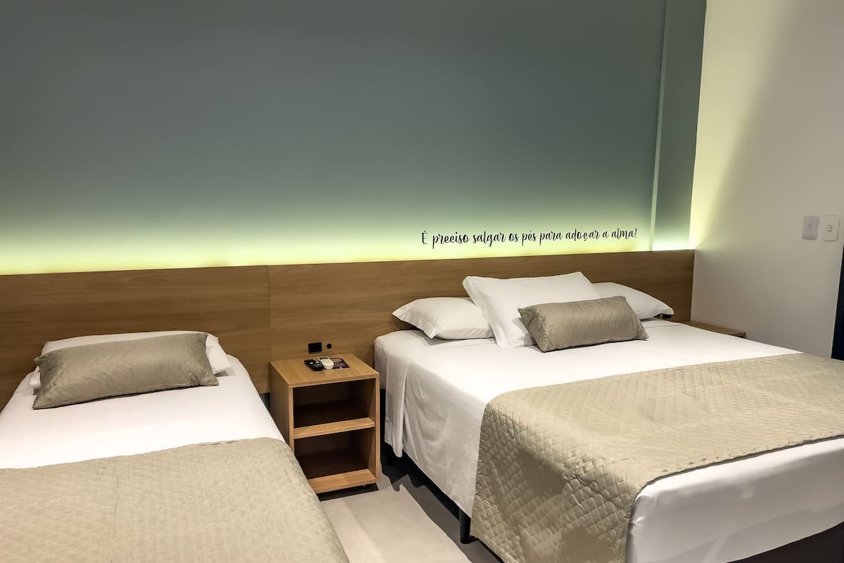 A hotel room with two beds, a nightstand, and a wall with a light.