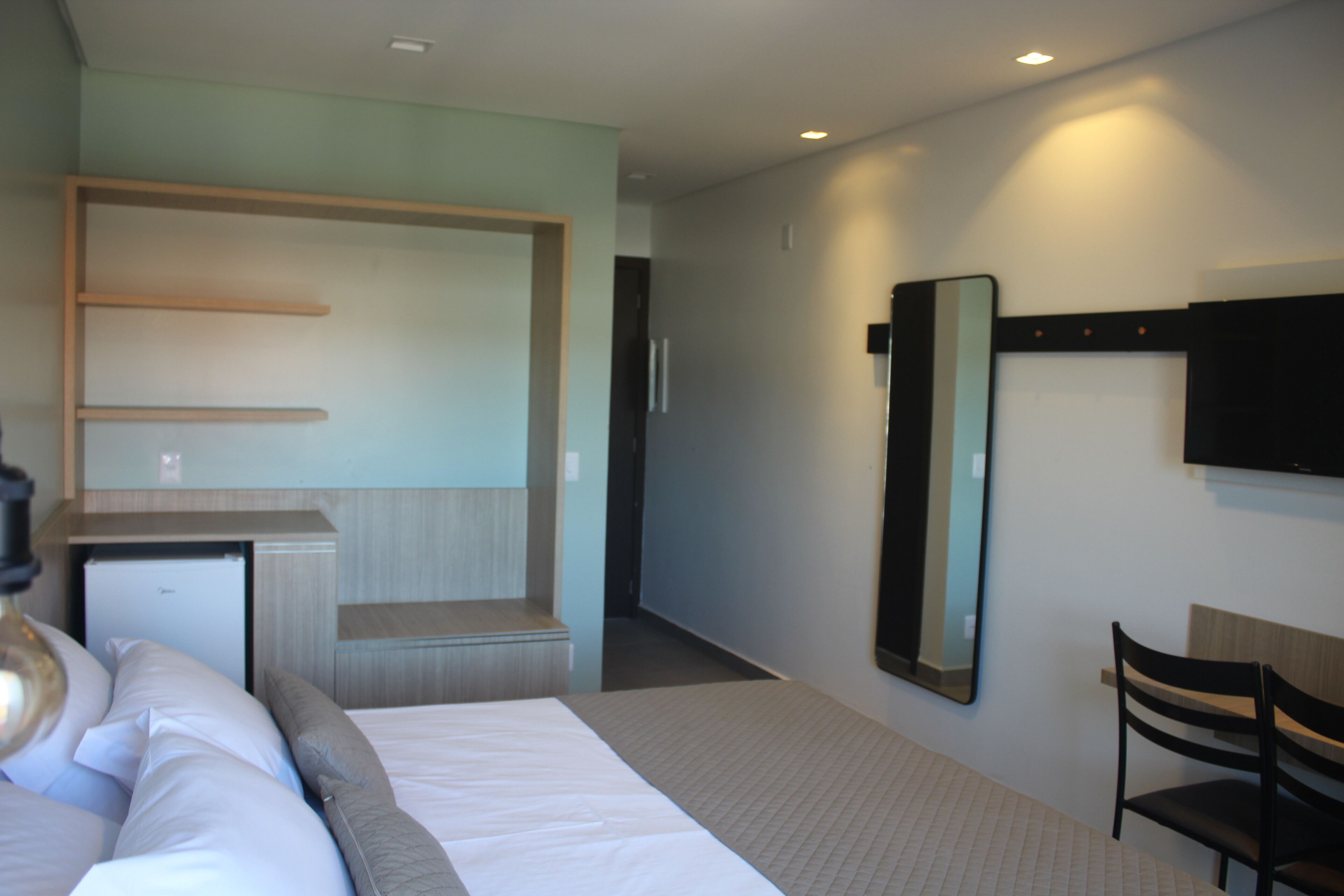 A hotel room with a bed, a desk, a chair, a mirror, and a television.