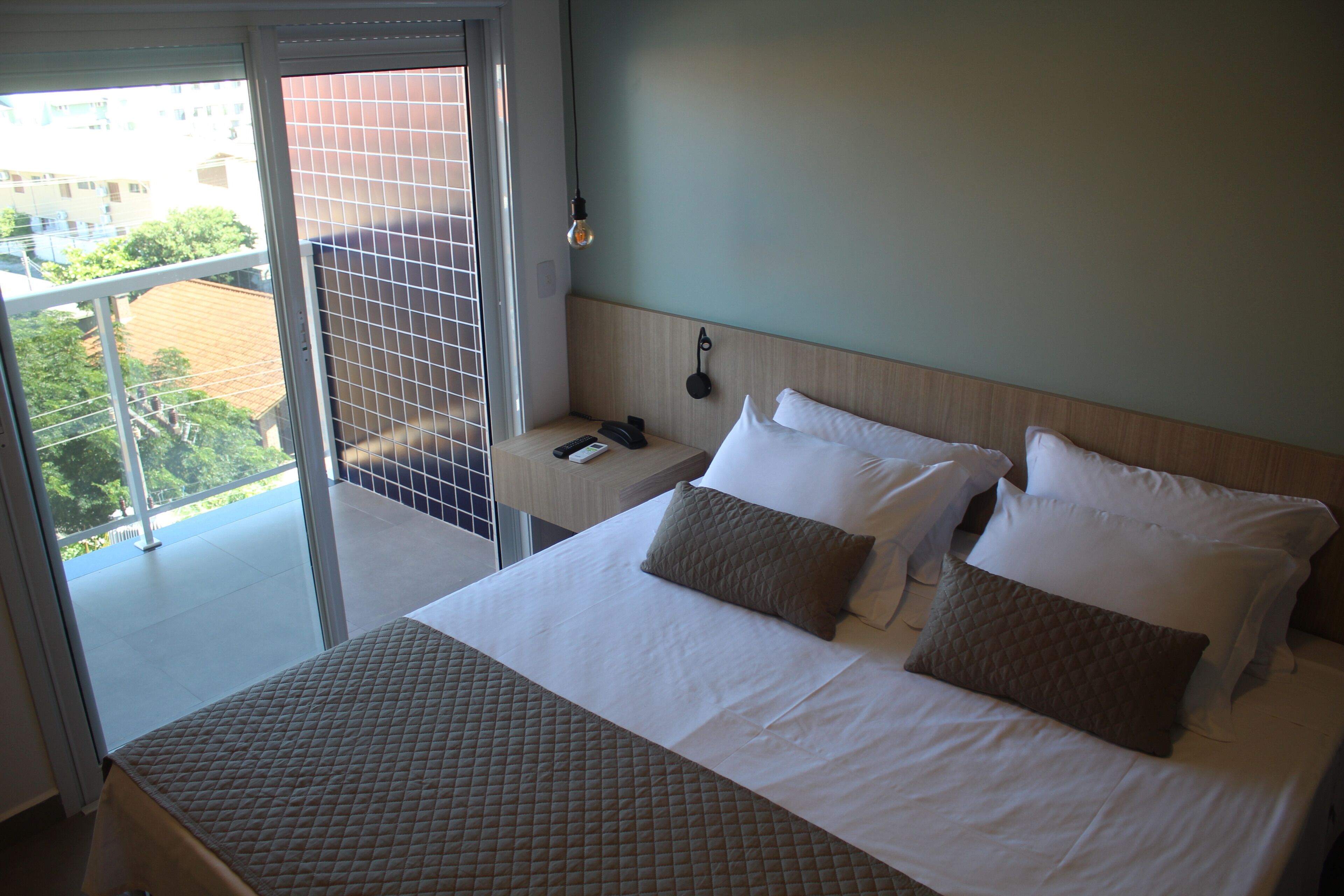 Una habitación de hotel con una cama, una mesita de noche, un teléfono y una lámpara en la pared.