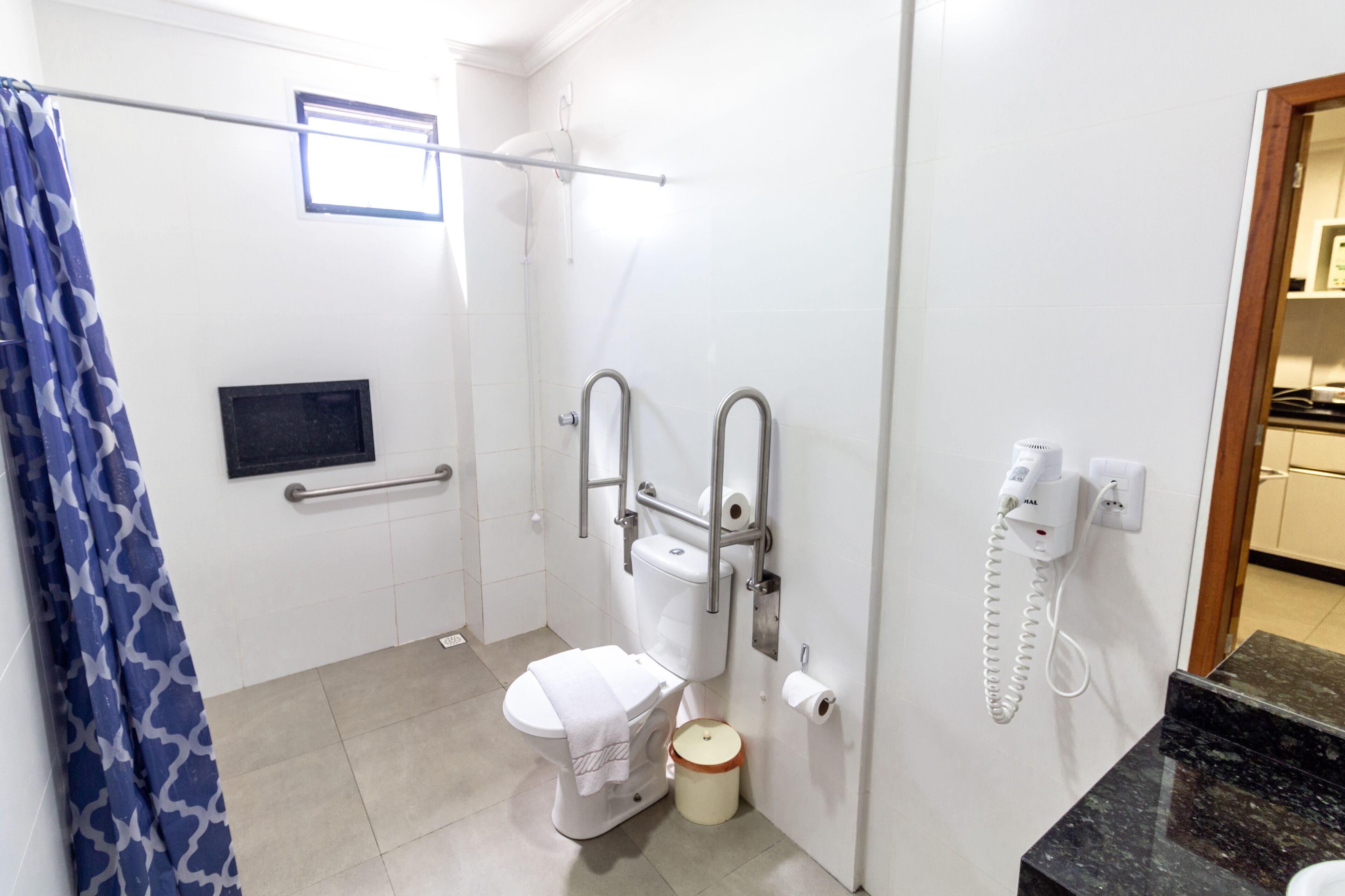 Un baño con inodoro, ducha, toallero, secador de manos y teléfono.