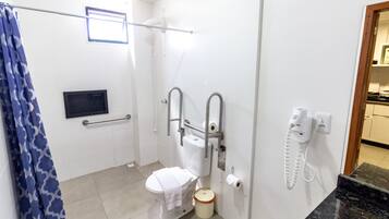 Un baño con inodoro, ducha, toallero, secador de manos y teléfono.