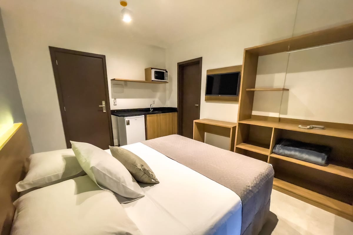 A hotel room with a bed, a desk, a TV, and a kitchenette.