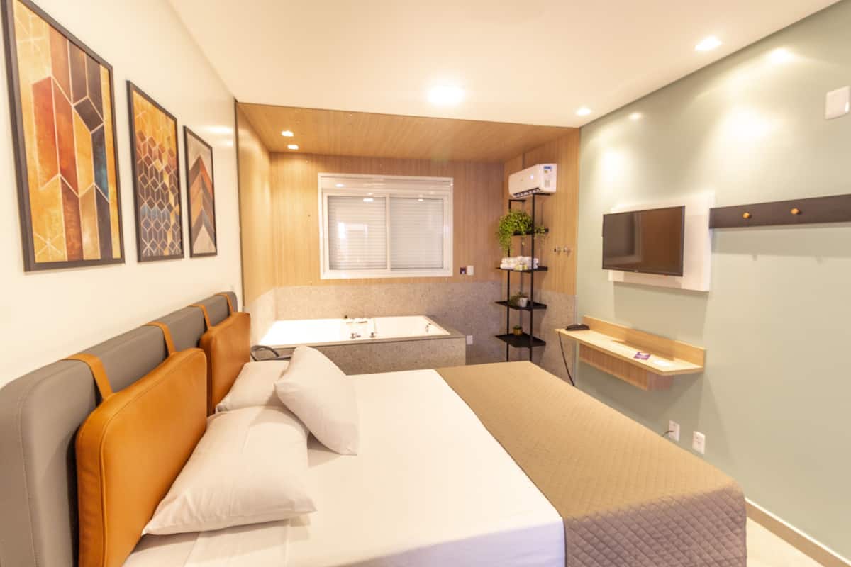 A hotel room with a bed, a small bathroom, a TV, and artwork on the wall.