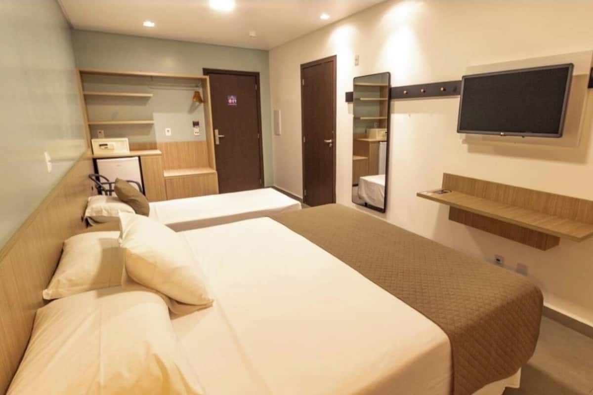 A hotel room with two beds, a TV, a mirror, and a kitchenette.