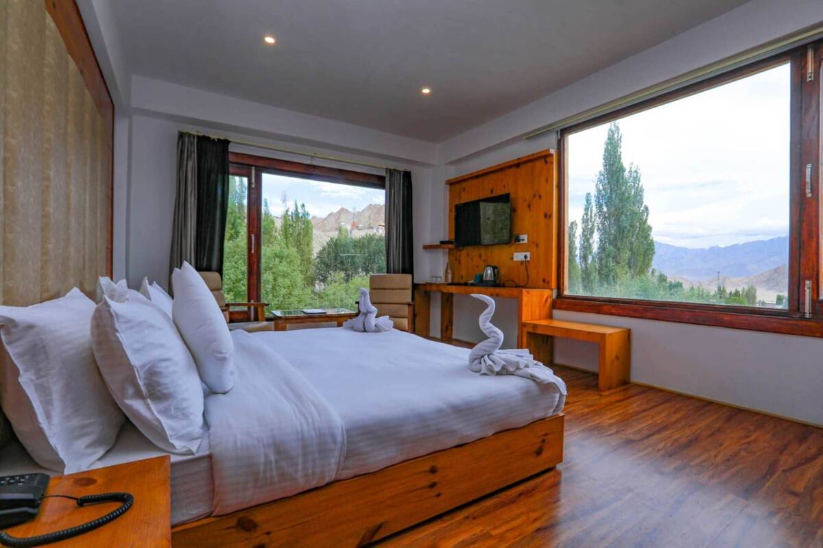 Un dormitorio con una cama grande, cabecera de madera, un escritorio de madera, televisión y vistas panorámicas por la ventana.