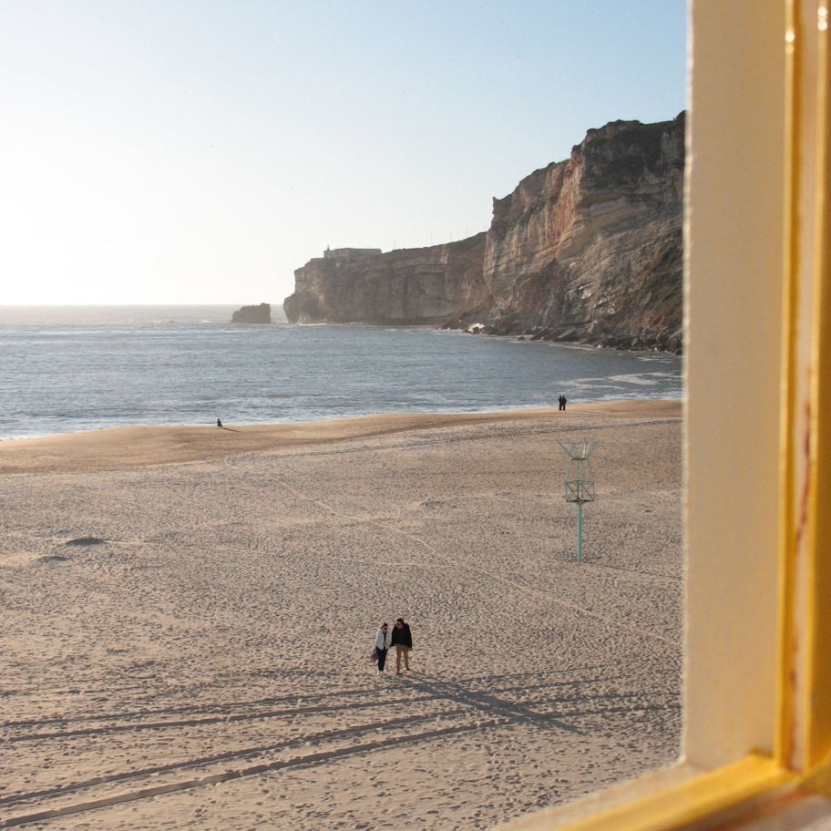 A beach with a person walking, cliffs in the background, and a clear sky.