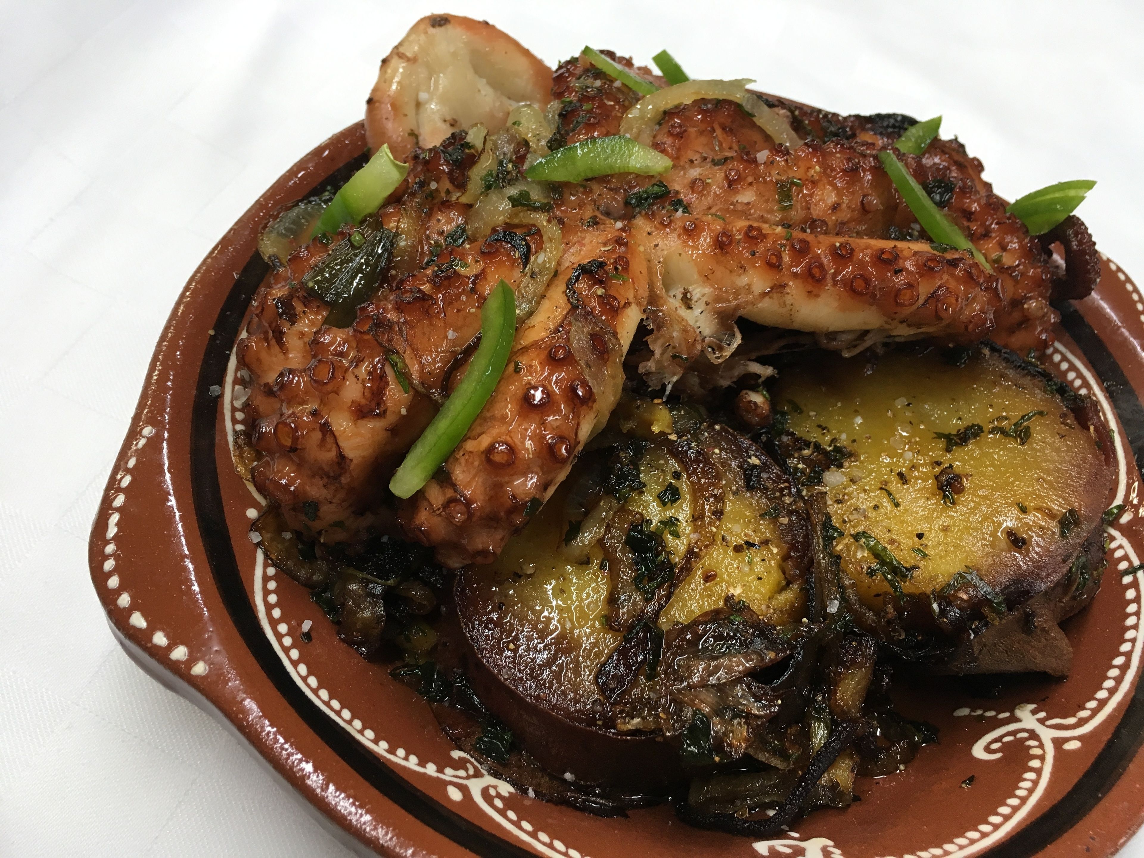A dish of grilled octopus with green peppers and onions on a decorative plate.