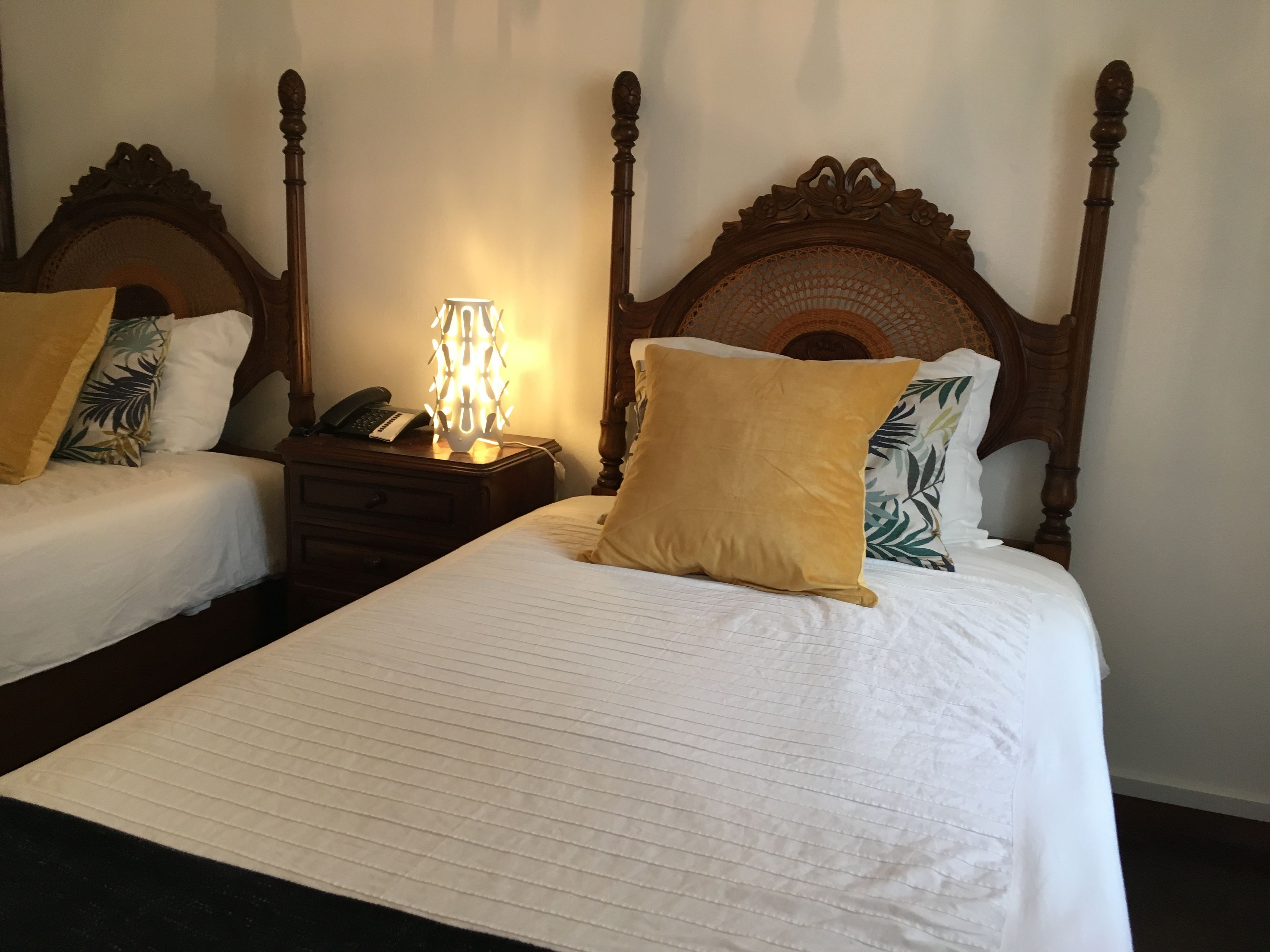 A hotel room with two beds, each with a wooden headboard, white linens, and a single bedside lamp.