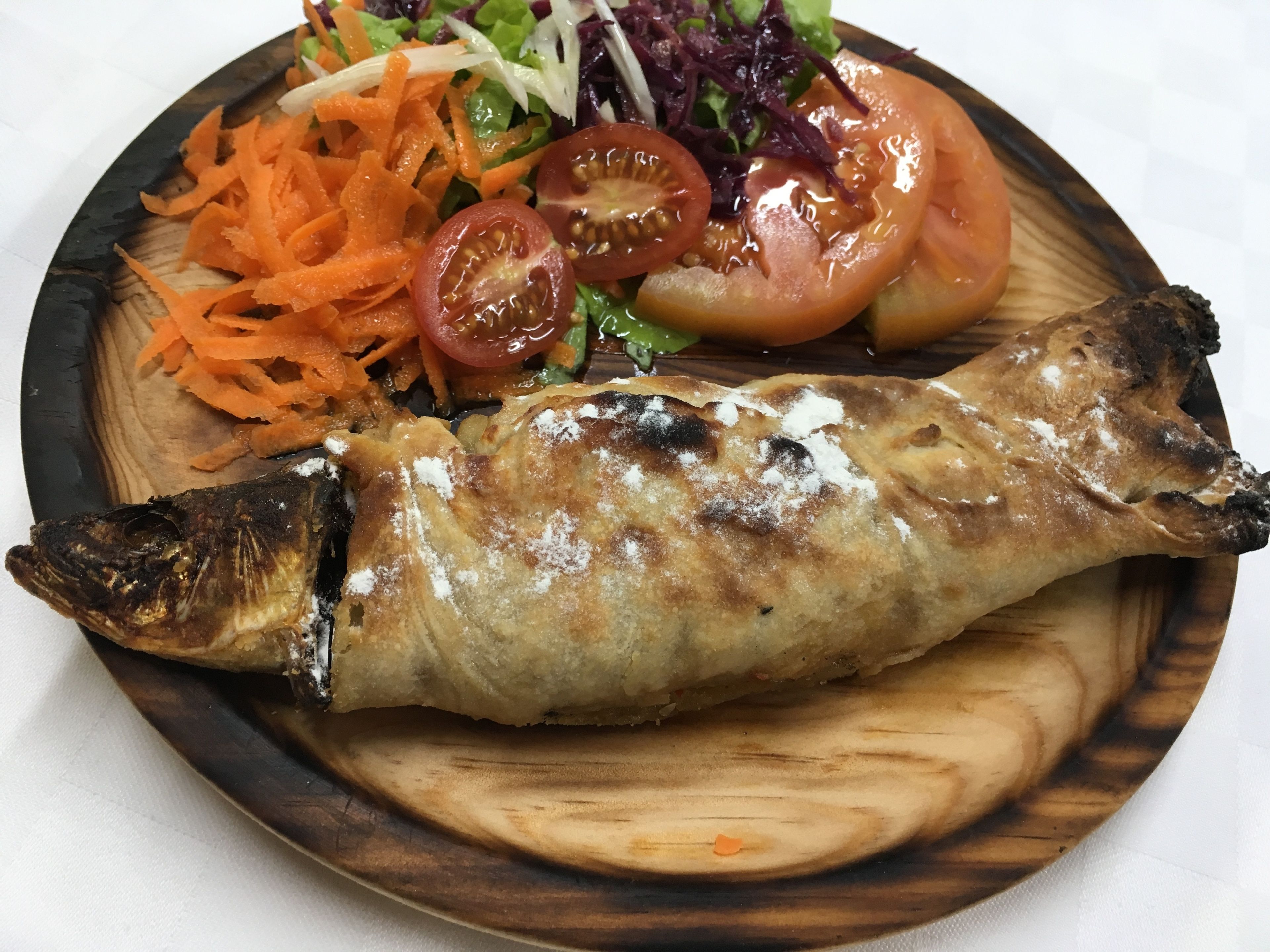 Une assiette contenant du poisson grillé, une salade et des tomates en tranches.