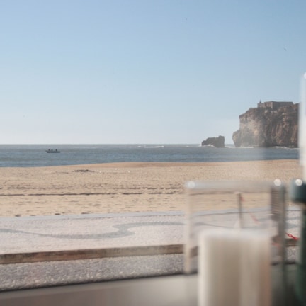 A coastal view with a sandy beach, a rocky cliff, and a small boat in the distance.