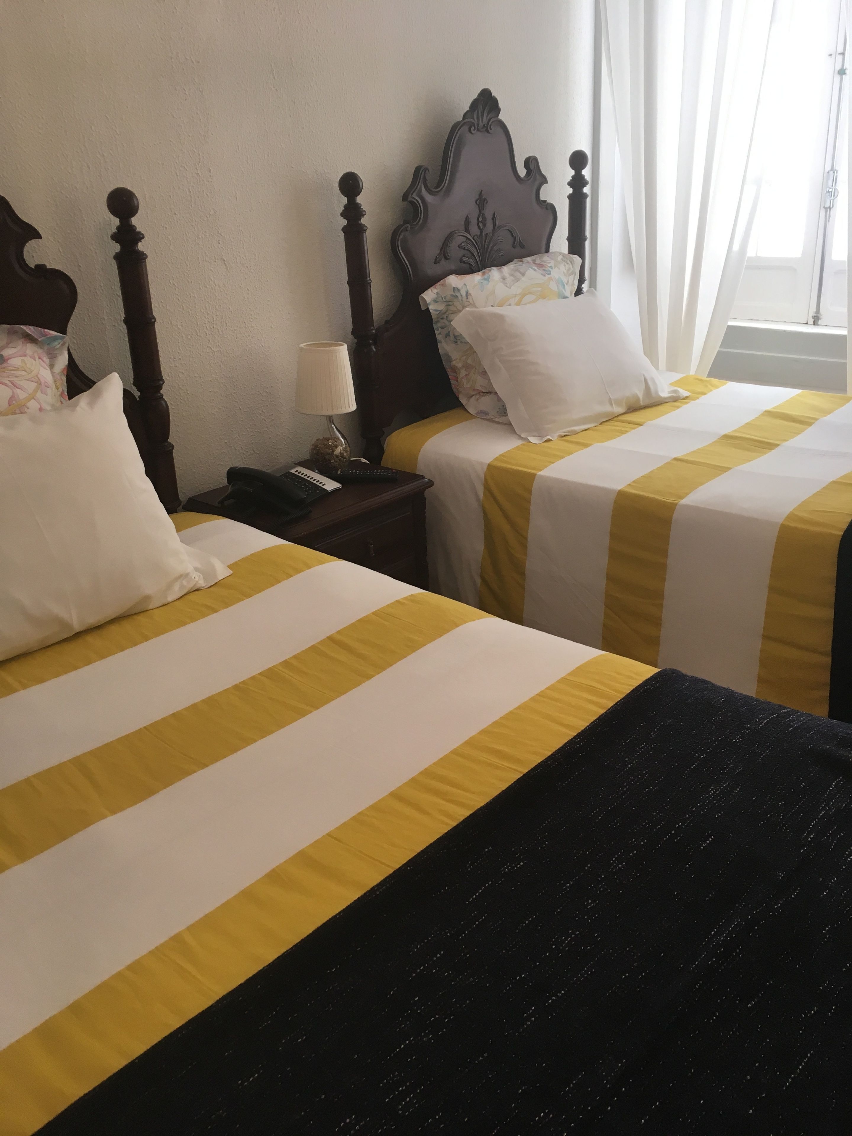 A hotel room with two beds, each with a striped bedspread, a wooden headboard, and a nightstand with a lamp and remote control.