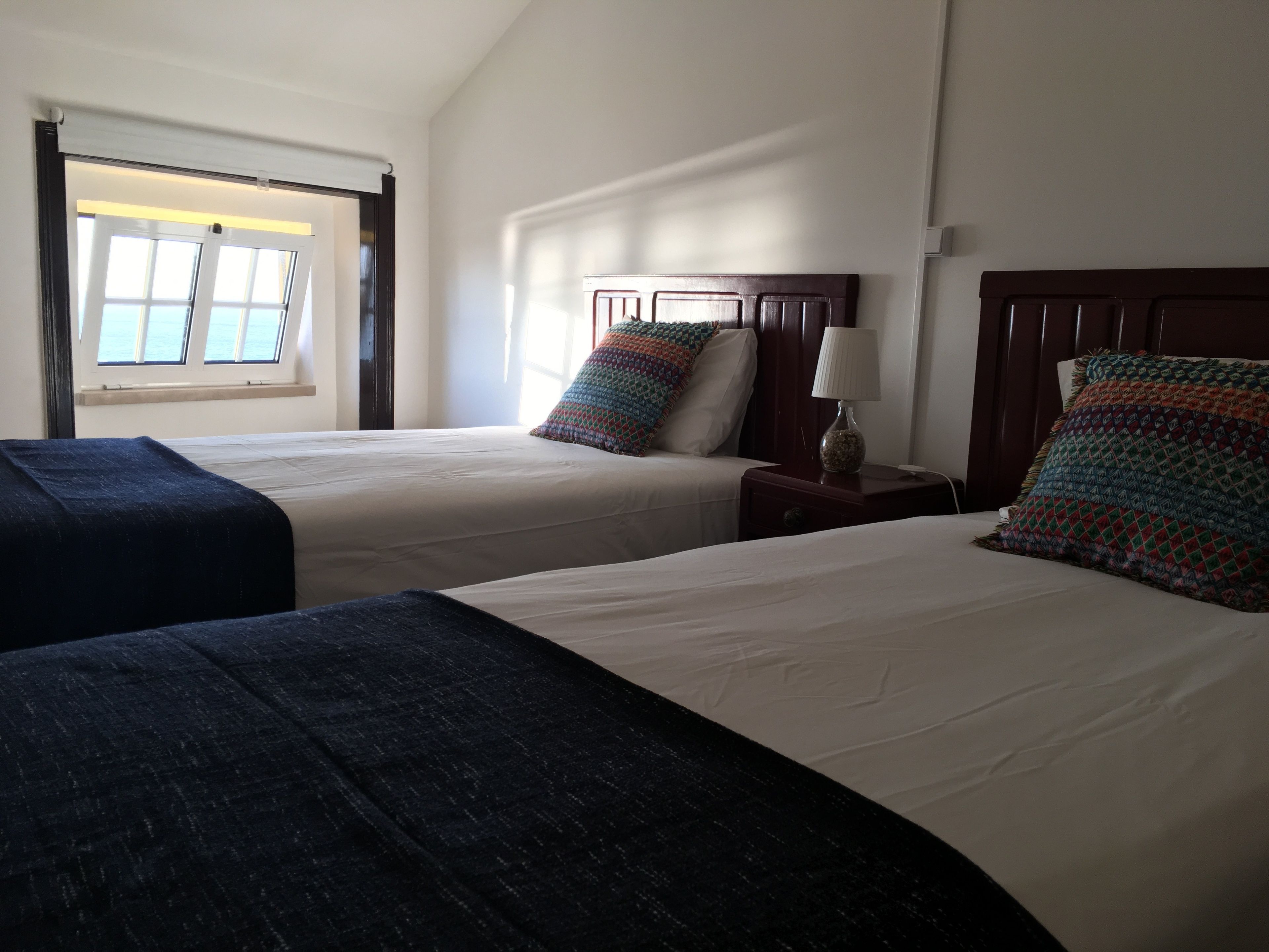 A hotel room with two beds, a window, and a nightstand with a lamp.
