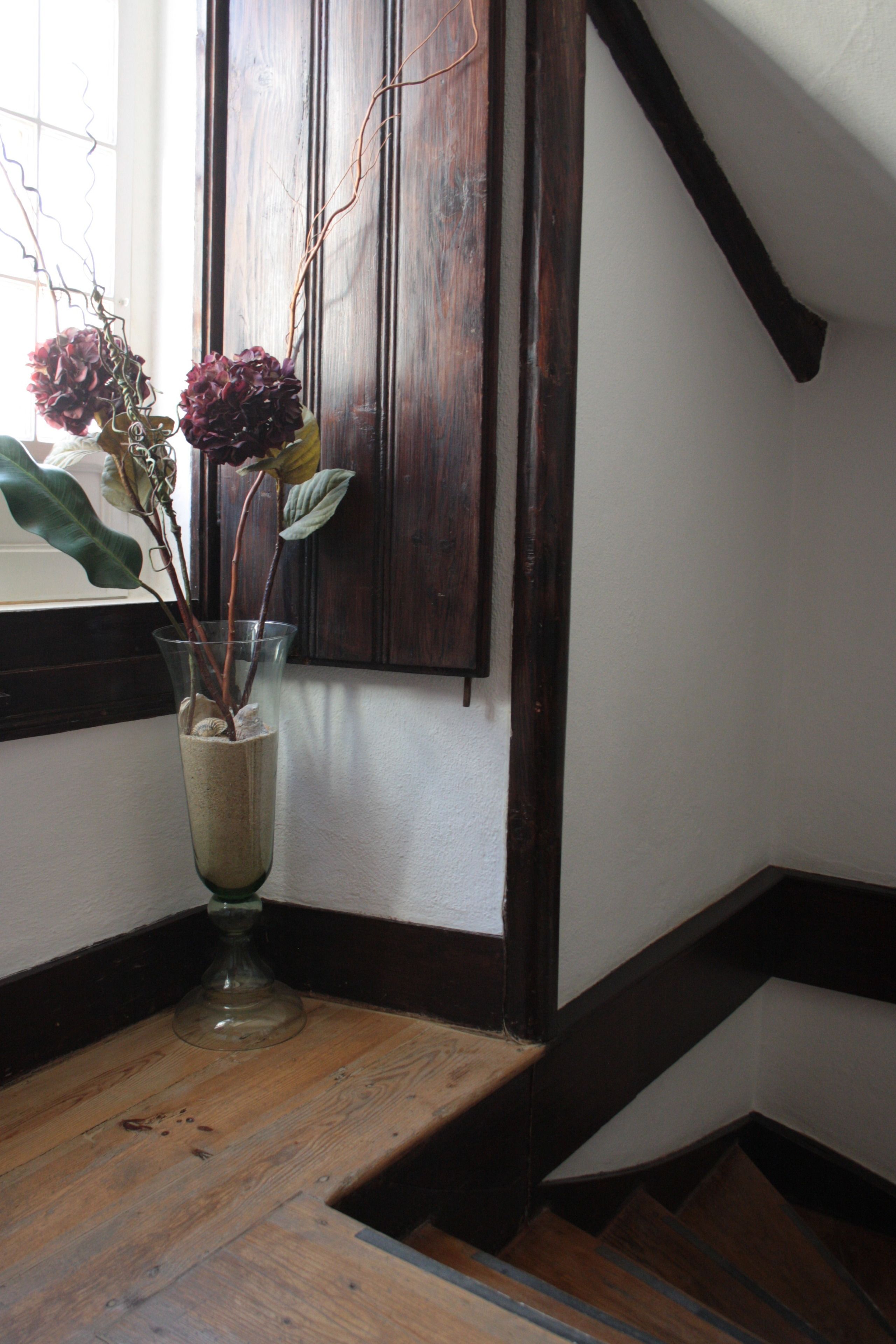 Una escalera con escalones de madera y un jarrón de vidrio con flores secas sobre un repisa de madera.