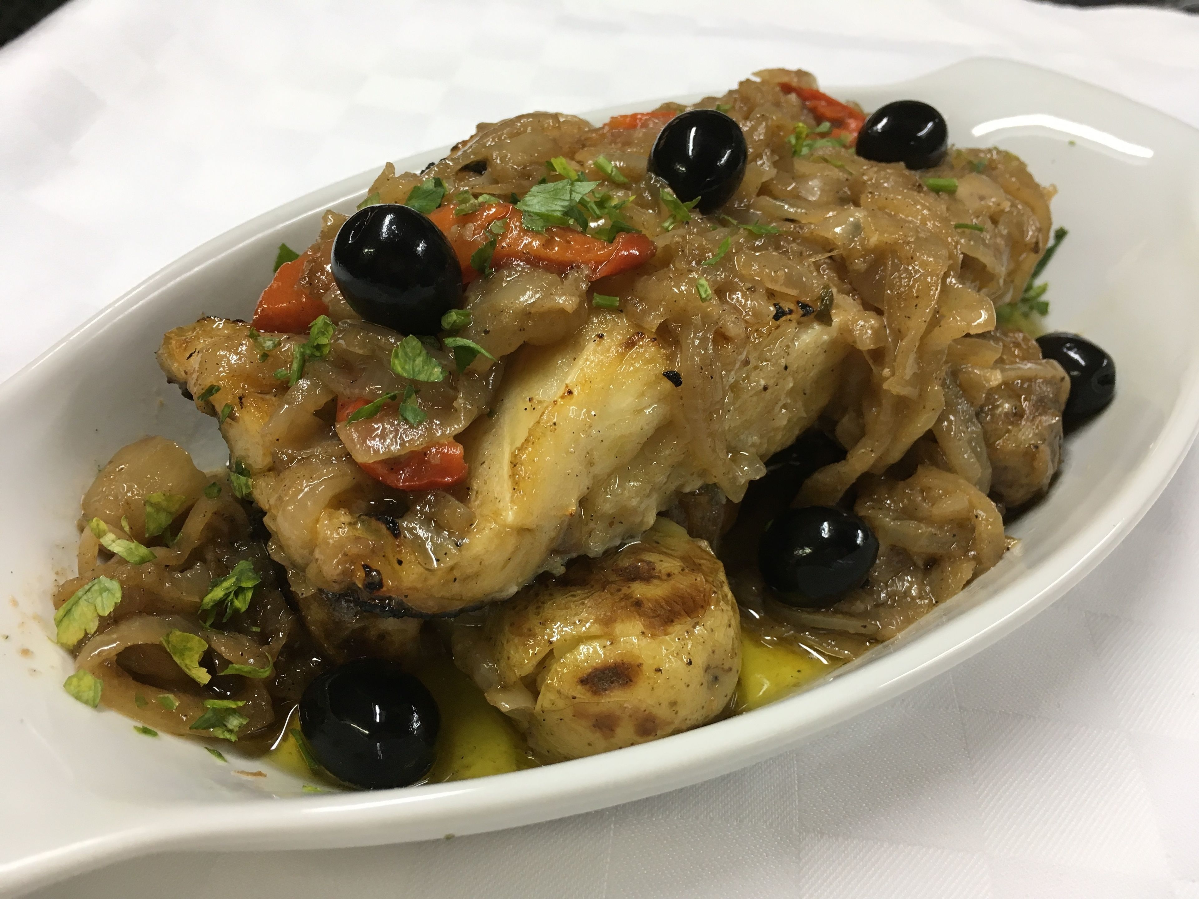 A dish of chicken with vegetables and olives on a white plate.