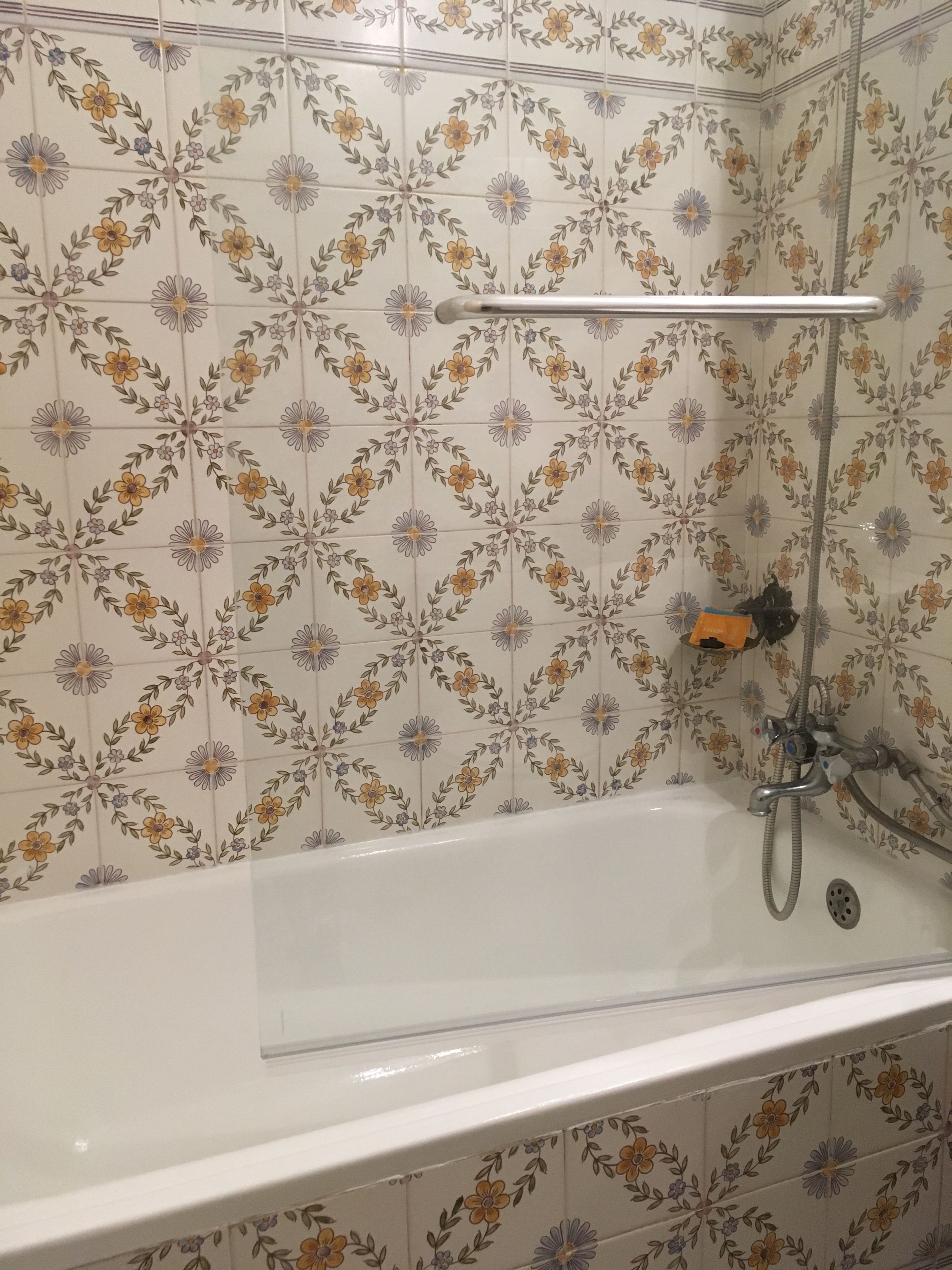 Un baño con baldosas de estampado floral, una bañera y una ducha con manguera.
