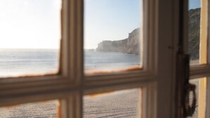 A view through a window with a wooden frame, overlooking a beach with cliffs in the distance. - Hotel Ribamar (Nazaré)