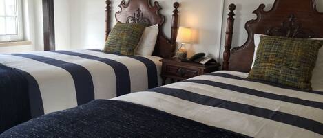 Two double beds with striped bedding, a wooden headboard, a bedside table with a lamp, and a telephone.