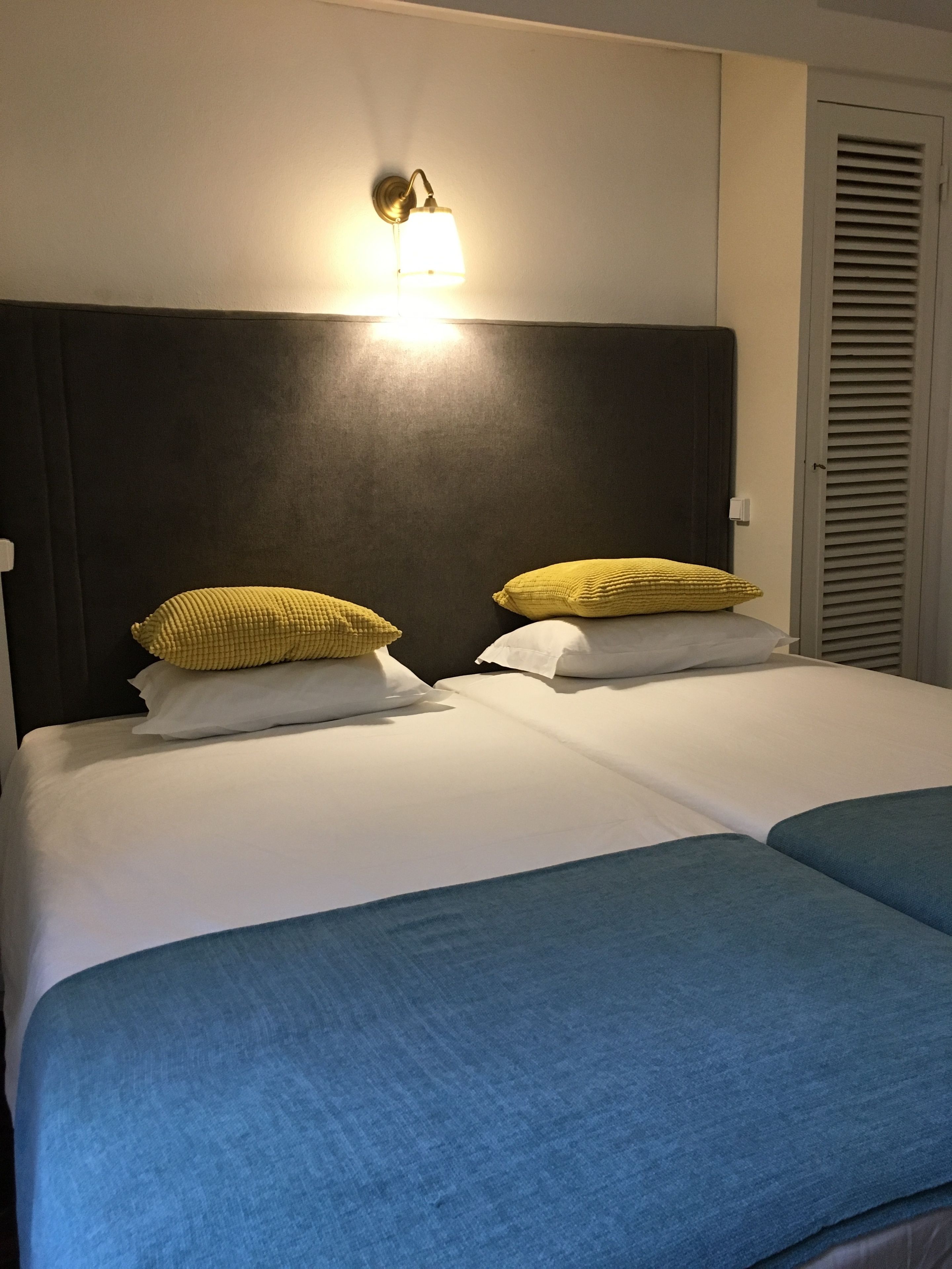Una habitación de hotel con una cama grande, dos almohadas, un cabecero y una lámpara fijada a la pared.