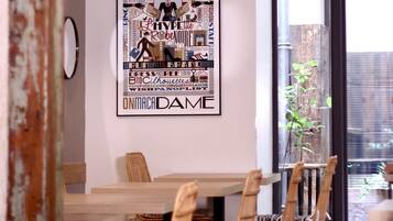 Un coin repas avec une table en bois et des chaises en osier, une œuvre d’art murale encadrée, et une vue sur l’extérieur à travers une porte vitrée.