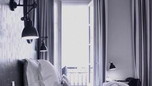 A modern hotel room with a neatly made bed, a nightstand with a lamp, and a view of the outdoors through a large window. - Hôtel de Tourny (Bordeaux)