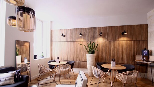 A modern lounge with wooden panel walls, wicker chairs, and a large potted plant. - Hôtel de Tourny (Bordeaux)