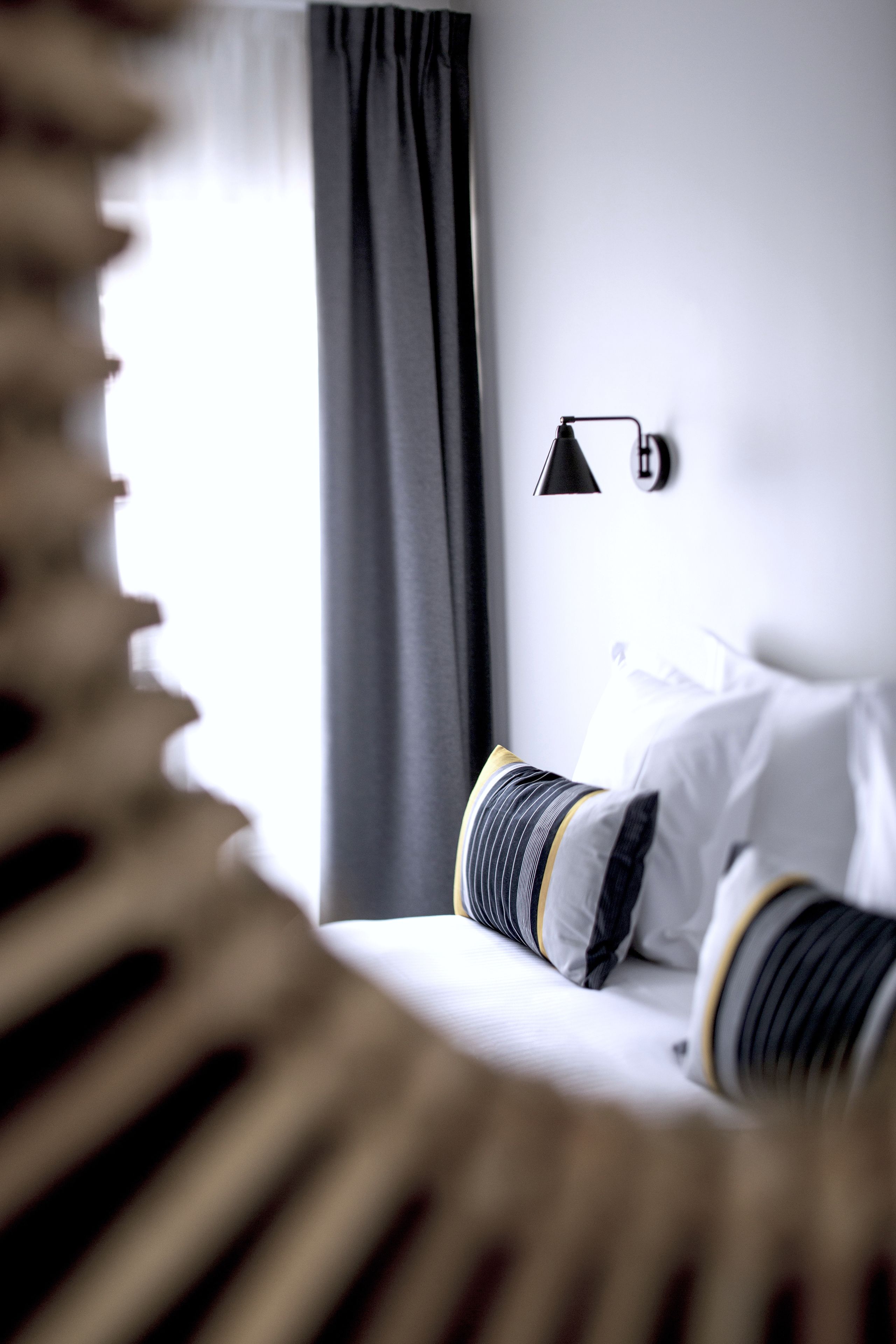 A hotel room with a bed, a bedside lamp, and a window with curtains.