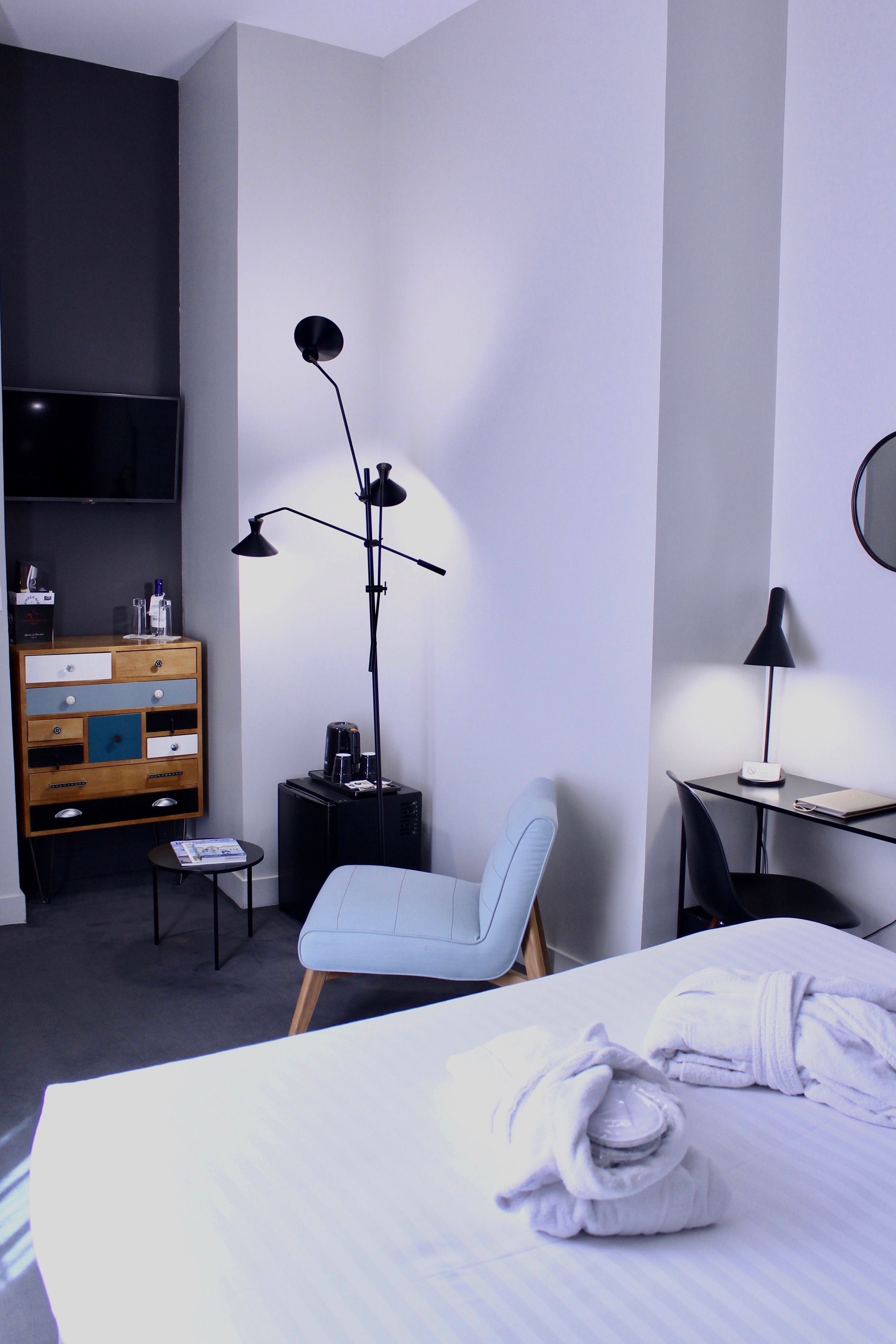 Quarto de hotel com cama, escrivaninha, cadeira, televisão, cômoda e luminária de chão.