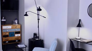 Quarto de hotel com cama, escrivaninha, cadeira, televisão, cômoda e luminária de chão.