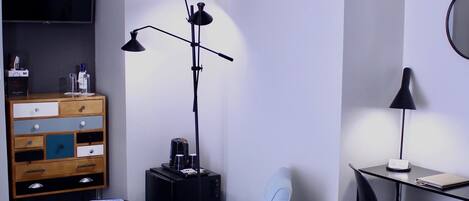 Habitación de hotel con cama, escritorio, silla, televisor, cómoda y lámpara de pie.