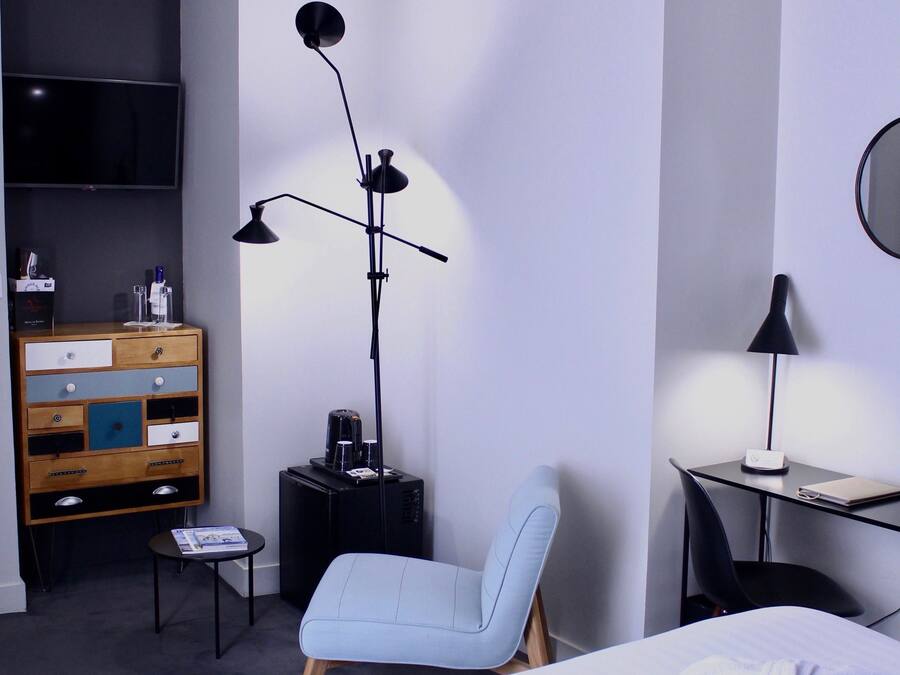 Quarto de hotel com cama, escrivaninha, cadeira, televisão, cômoda e luminária de chão.